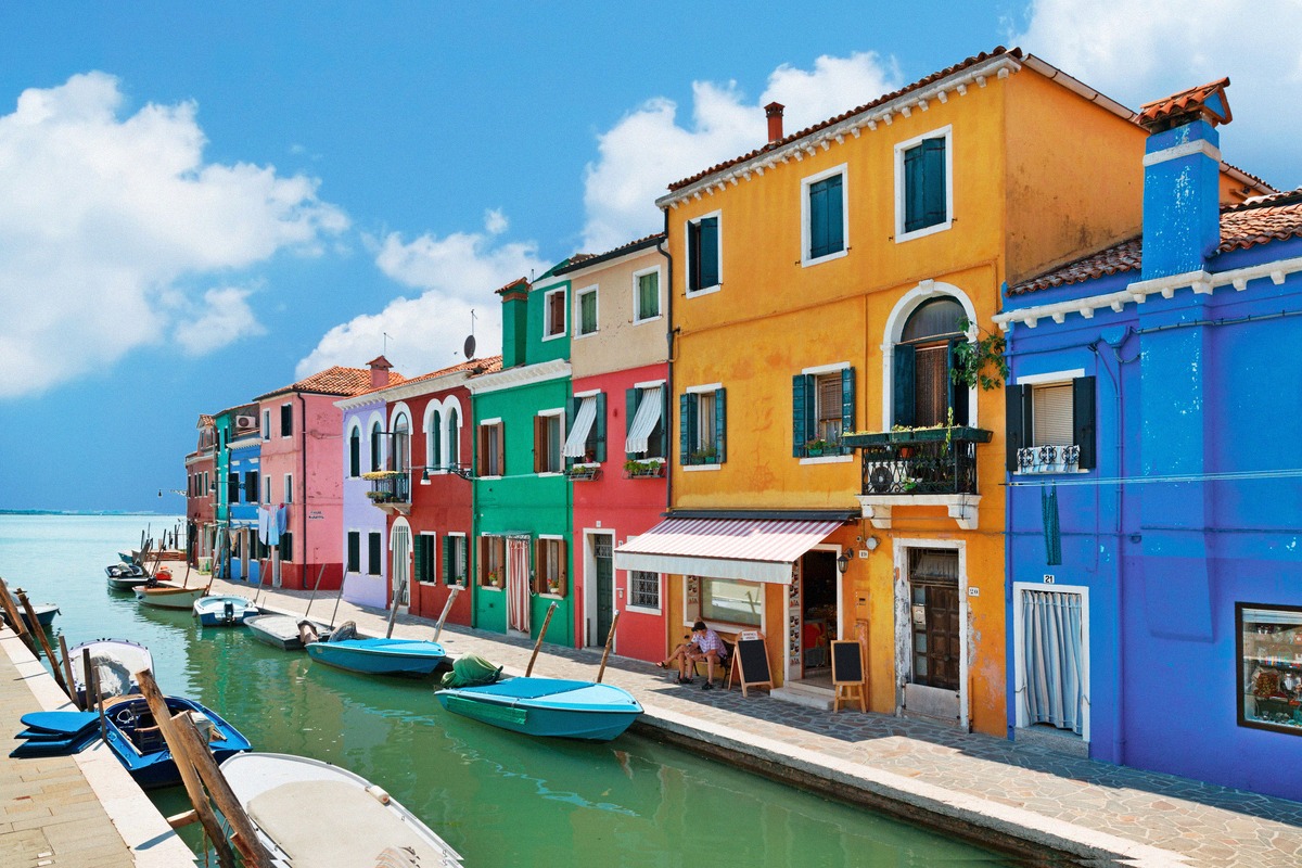 Die bunt gestrichenen Fischerhäuser von Burano säumen einen Kanal mit vertäuten Booten in der Lagune von Venedig