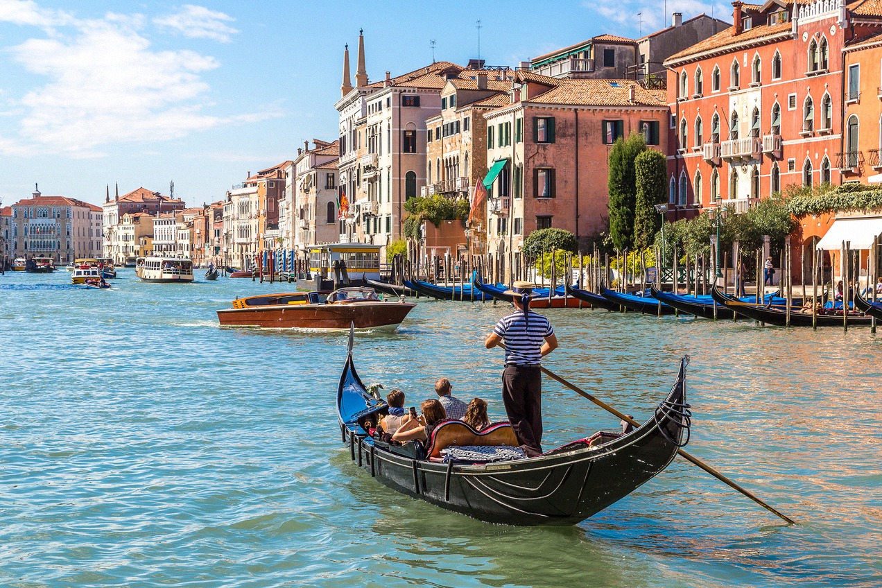 Gondel mit Touristen auf dem Canal Grande in Venedig, im Hintergrund die bunten Palazzi-Fassaden und weitere Boote auf dem Wasser